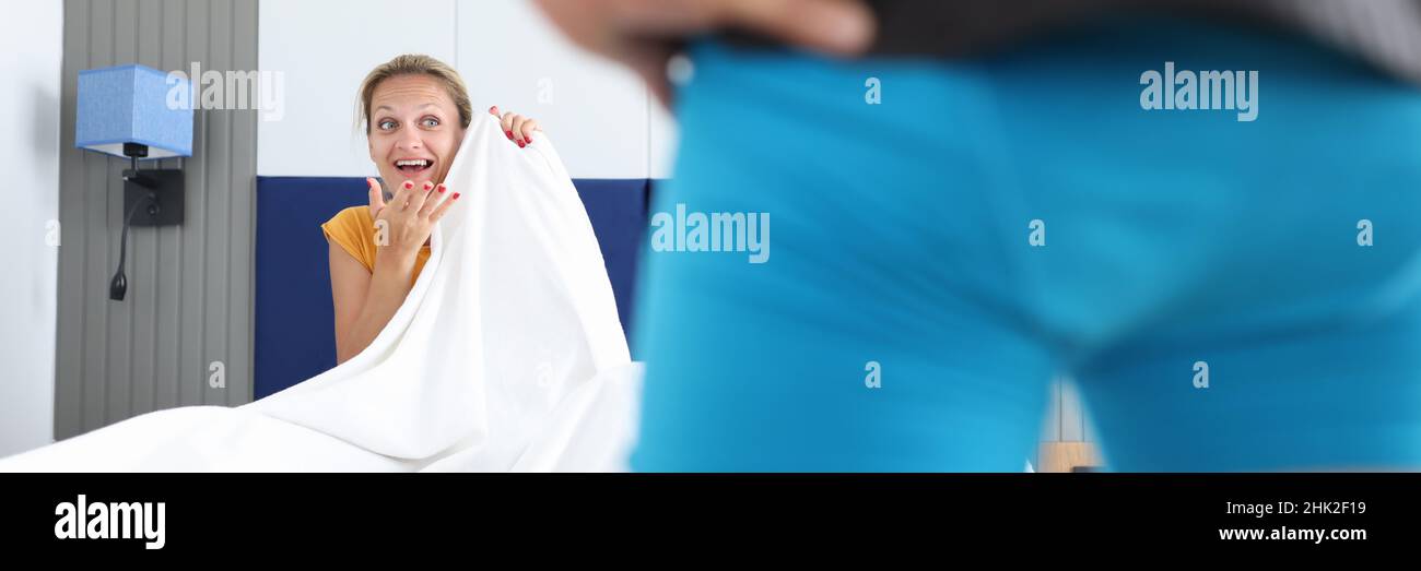 Frau, die auf dem Bett sitzt, sieht den Mann in kurzen Hosen aus der Nähe an Stockfoto