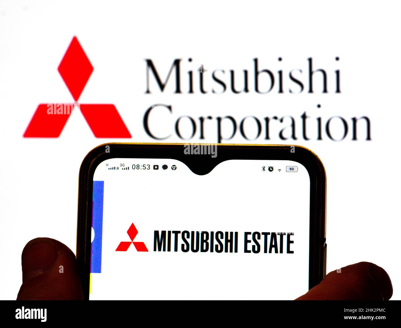 In dieser Abbildung wird das Mitsubishi Estate-Logo auf einem Smartphone-Bildschirm mit einem Mitsubishi Corporation-Logo im Hintergrund angezeigt. Stockfoto