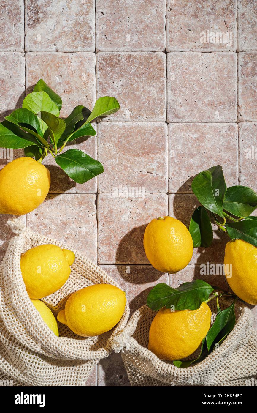 Frische sizilianische Bio-Zitronen mit grünen Blättern in Baumwolltasche auf Natursteinfliesen Hintergrund, sonniges Licht mit Schatten flach legen, Draufsicht. Eco Stockfoto