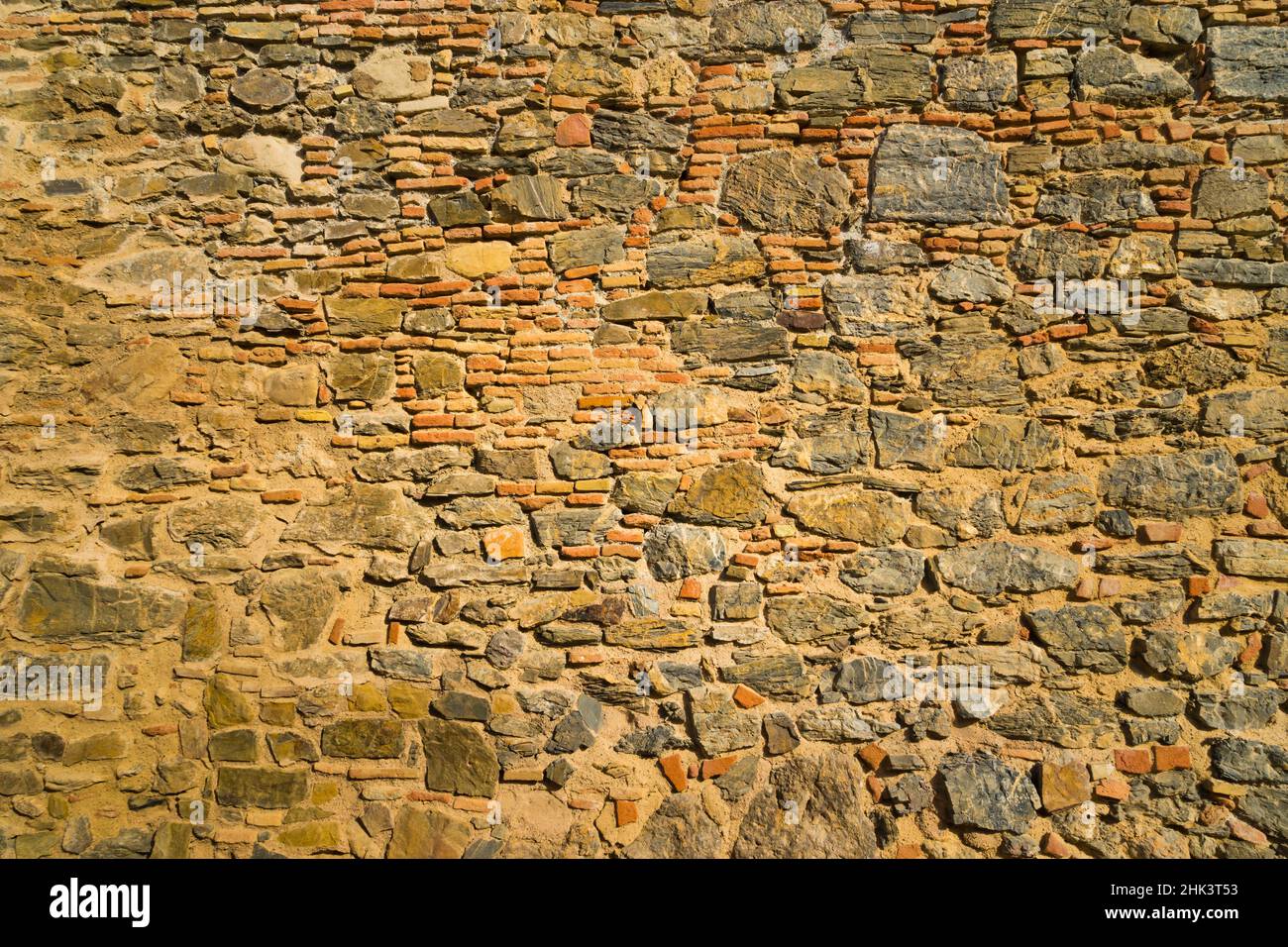 Ziegel- und Steinmauer in warmen Tönen einer alten mittelalterlichen Mauer. Konzept mit stark texturierten Hintergründen. Stockfoto