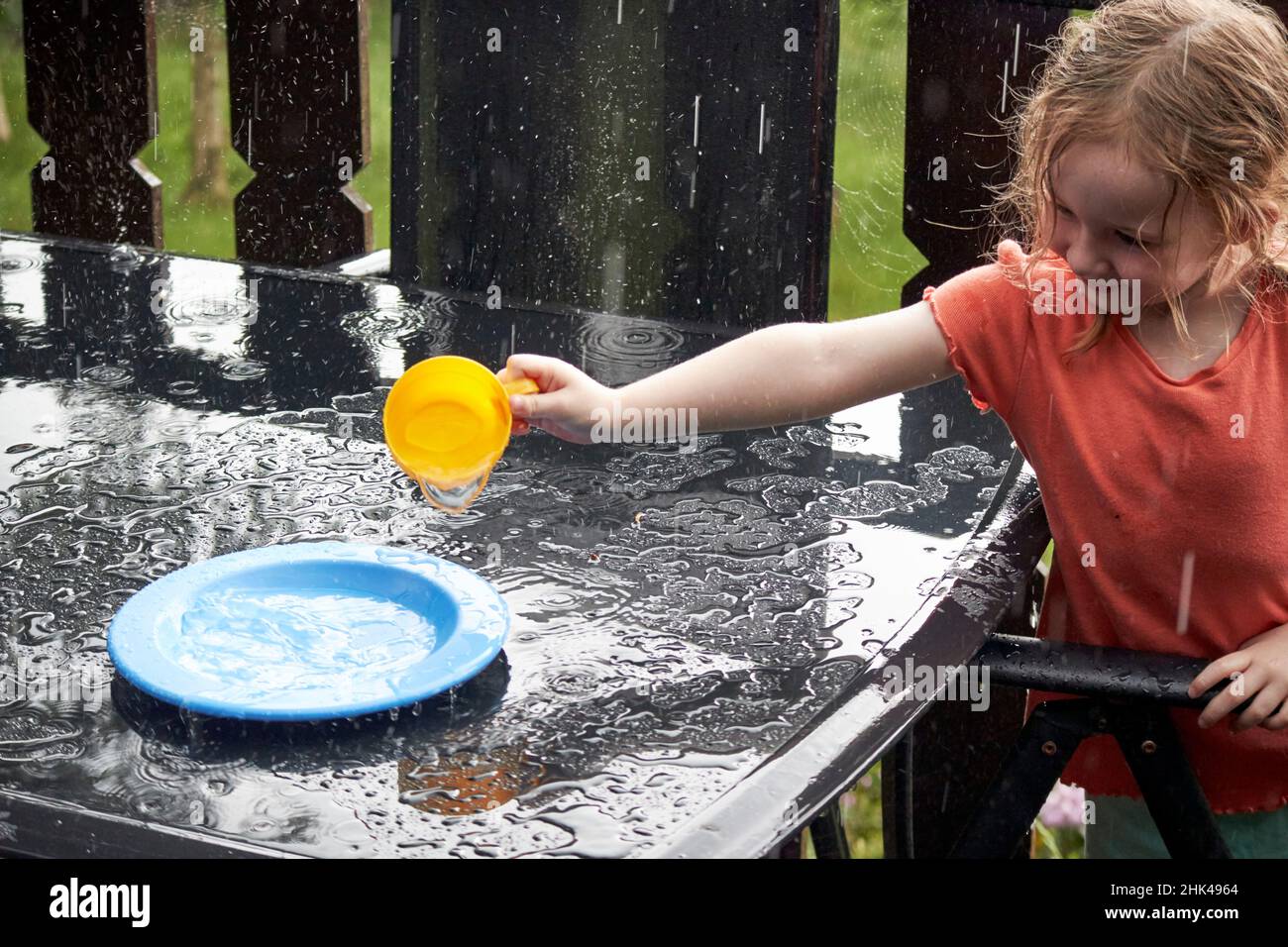 Das junge 4-jährige Mädchen spielt während des Regenguß im britischen Sommer im Lake District in großbritannien mit Wasser und Geschirr Stockfoto