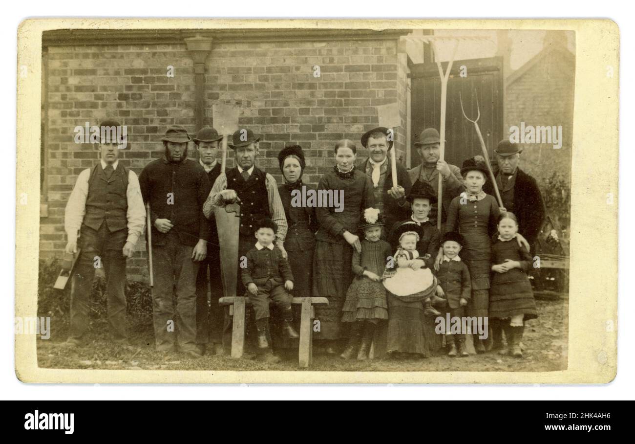 Wunderbare viktorianische Carte de Vistie (CDV) oder Visitenkarte von Gruppenarbeitern und ihren Familien - Frauen und Kinder, mehrere Charaktere auf viktorianischer Farm. Alle sind in dem gekleidet, was ihr einziges Kleidungsstück gewesen wäre - ihre sonntäglichen besten. Die Männer tragen Bowler-Hüte, um ihre Köpfe zu schützen. Für das Foto mit den Werkzeugen ihres Fachs posieren: Wartungsteam mit Holzbearbeitungswerkzeugen, Spaten und einer Pistole und Bauernhände mit ihren landwirtschaftlichen Werkzeugen - Pitinerant Gabel, Spaten und Rechen, von dem Wanderfotografen A. (Alfred) Arnell aus Scarborough, Yorkshire, England, um 1880er Jahre Stockfoto