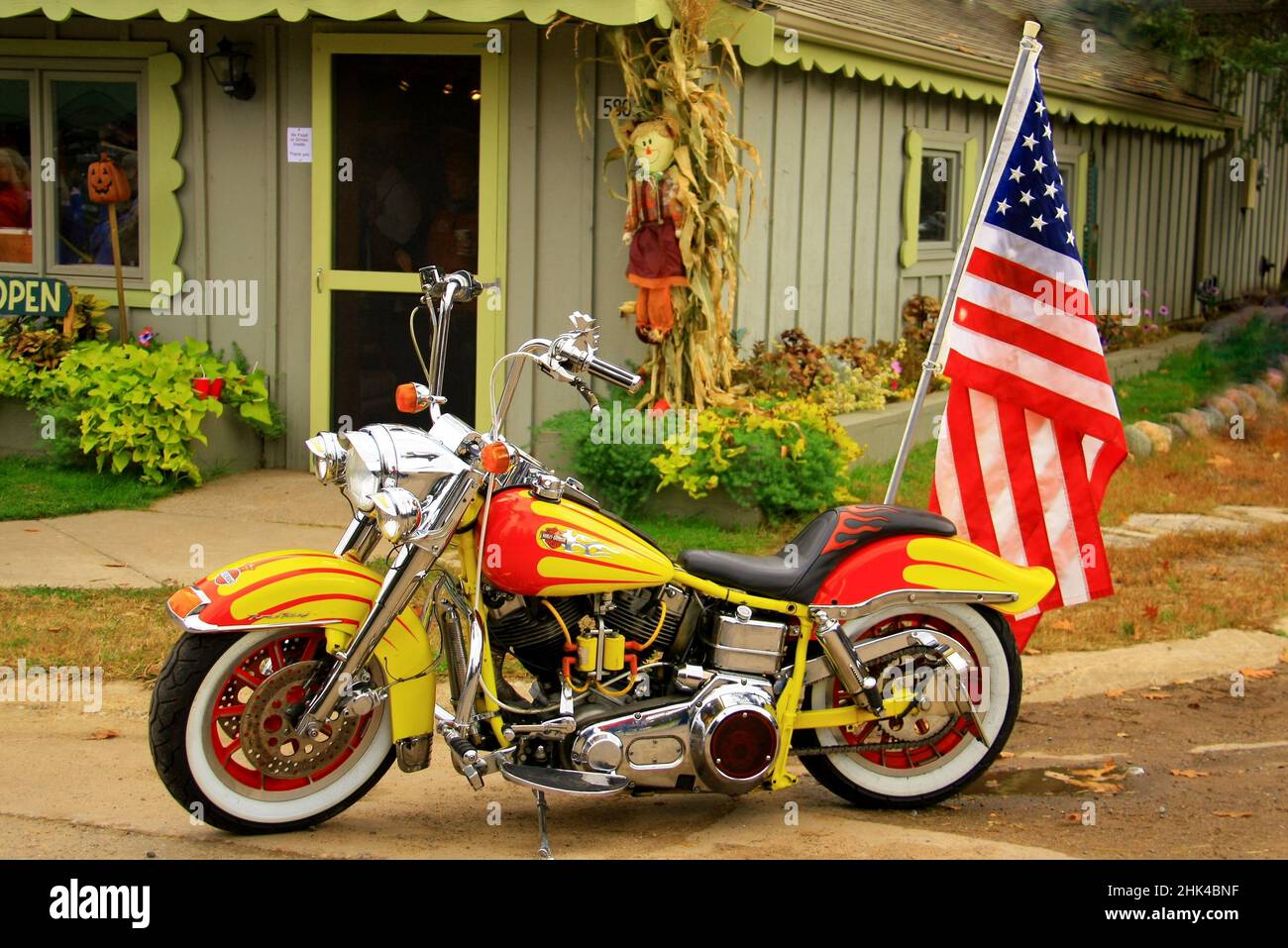 Orange und gelb Harley Davison Motorrad mit einer amerikanischen Flagge auf der Rückseite geparkt vor einem Geschäft für Herbst dekoriert. Stockfoto