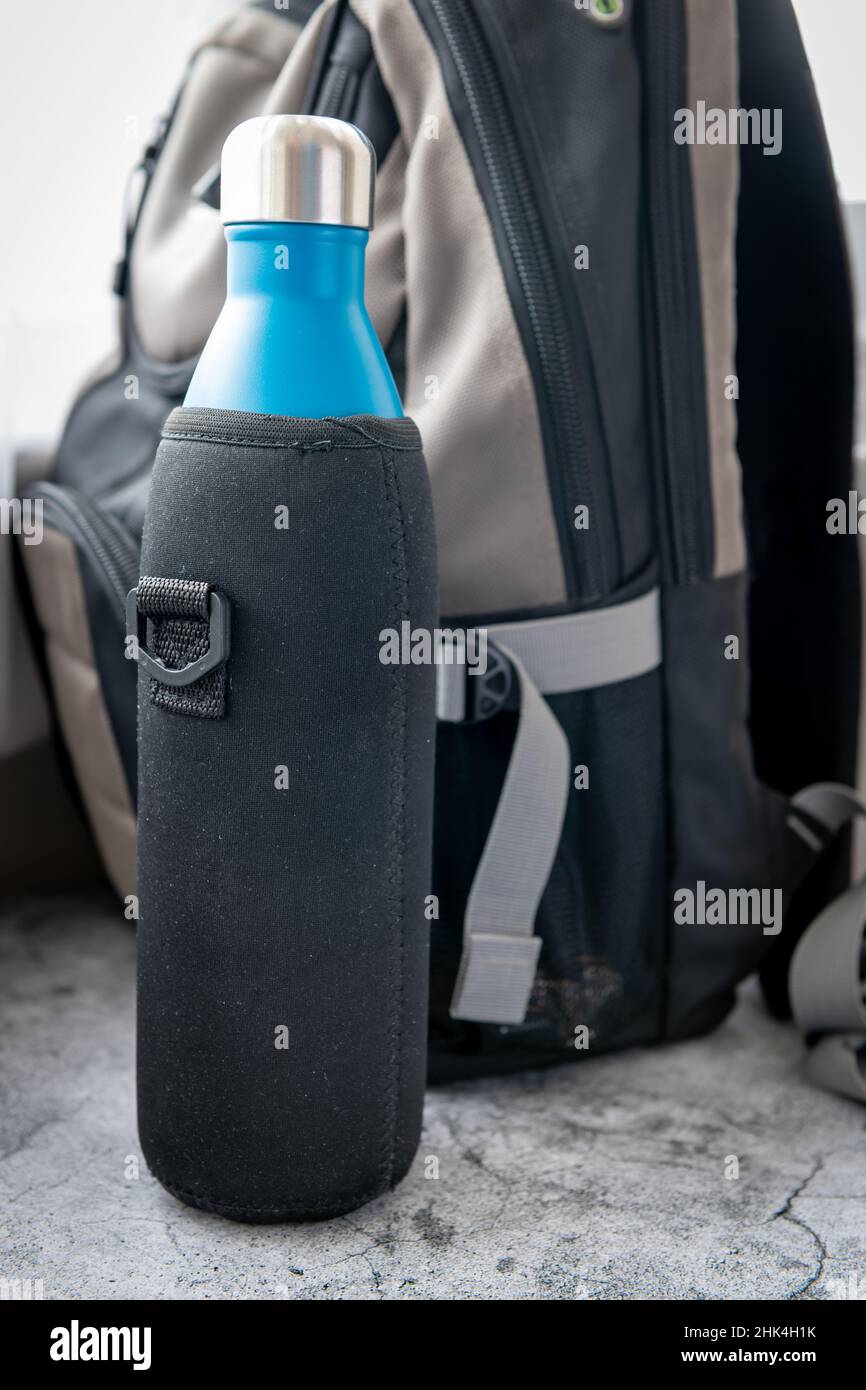 Eine isolierte wiederverwendbare Wasserflasche oder Thermoskanne vor einem Rucksack. Stockfoto