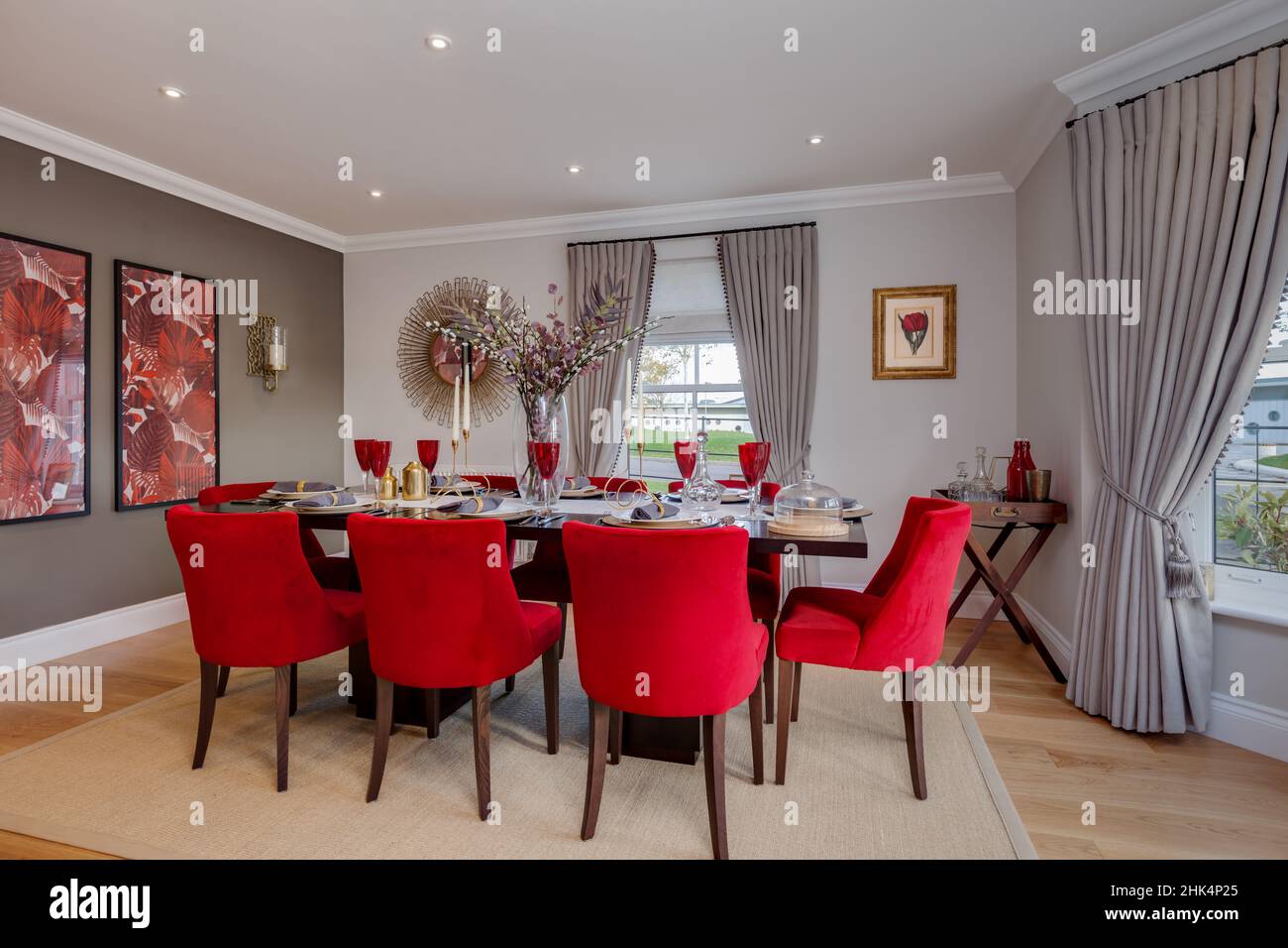 Alconbury Weald, Cambridgeshire - Oktober 17 2016: Beeindruckendes Esszimmer im modernen Luxushaus mit Tischstühlen, die mit hellrotem Stoff bezogen sind Stockfoto