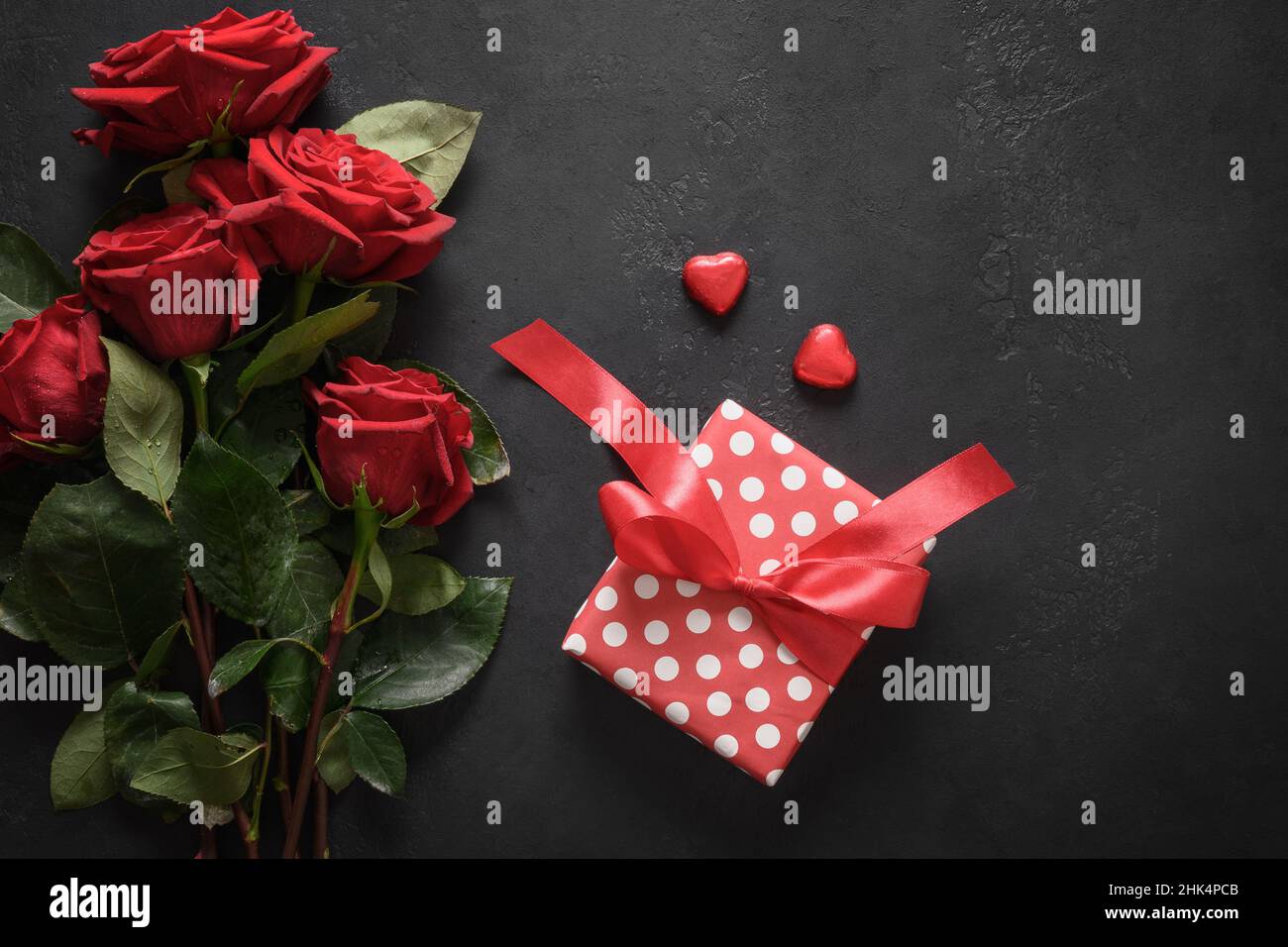 Valentinskarte mit Geschenk und roten Rosen auf schwarzem Hintergrund mit Platz zum Kopieren. Blick von oben. Stockfoto