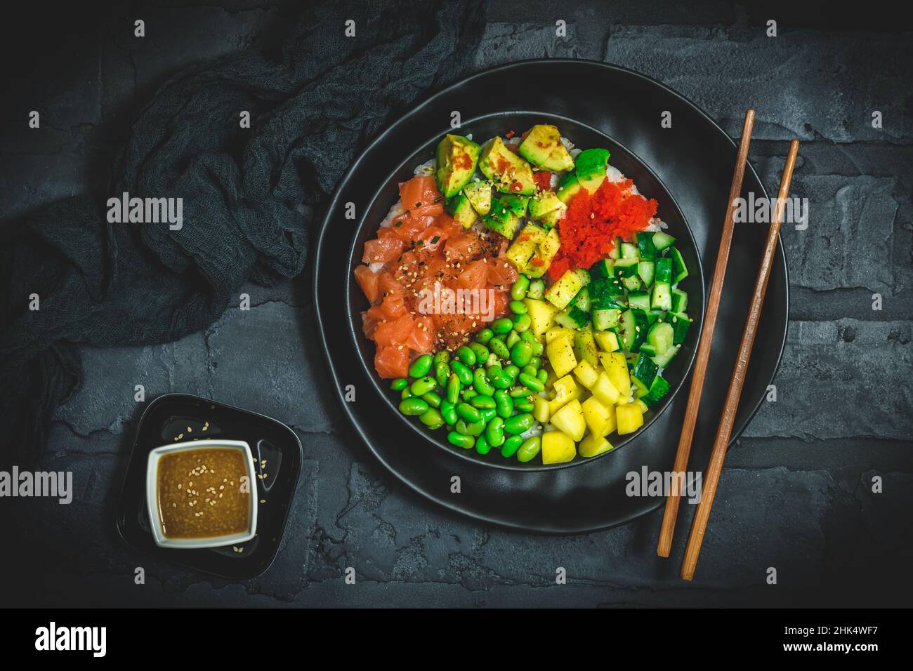 Japanische Poke- oder buddha-Schale mit Lachs, Avocado, Rogen, Mango, Pasteten und Gurke in einer schwarzen Schale auf schwarzem Hintergrund, Draufsicht Stockfoto