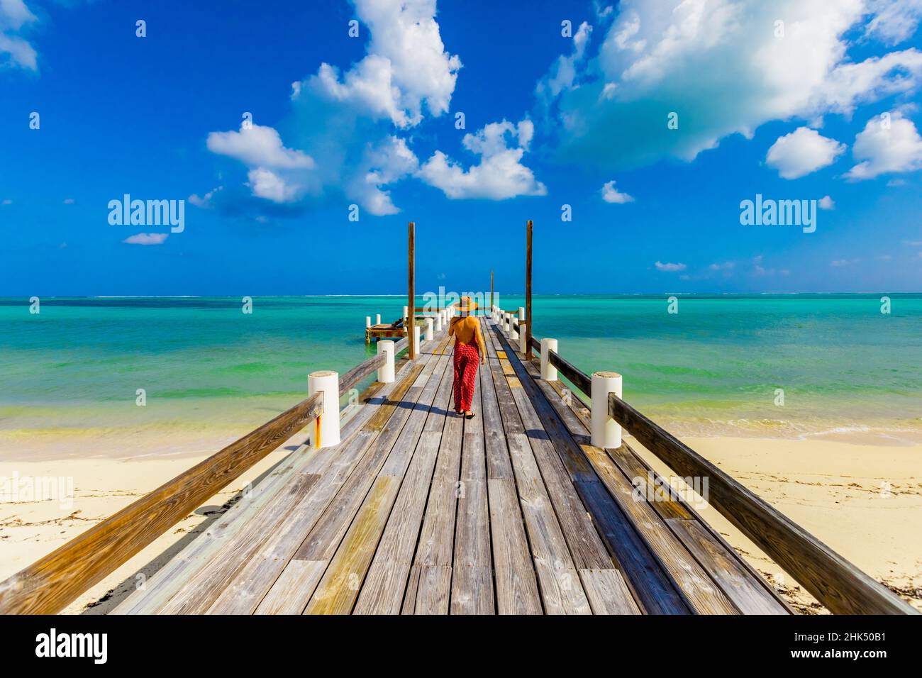 Frau, die vom Horse Stable Beach, North Caicos, Turks- und Caicos-Inseln, Atlantik und Mittelamerika aus den Pier hinaufgeht, der sich bis ins Meer erstreckt Stockfoto
