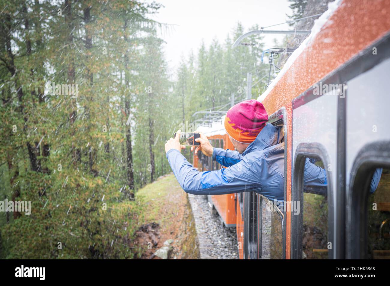 Mann, der den Schnee fotografiert, der über den Wald fällt und sich aus dem Zug der Gornergrat Bahn, Zermatt, Kanton Wallis, Schweiz, Europa lehnt Stockfoto