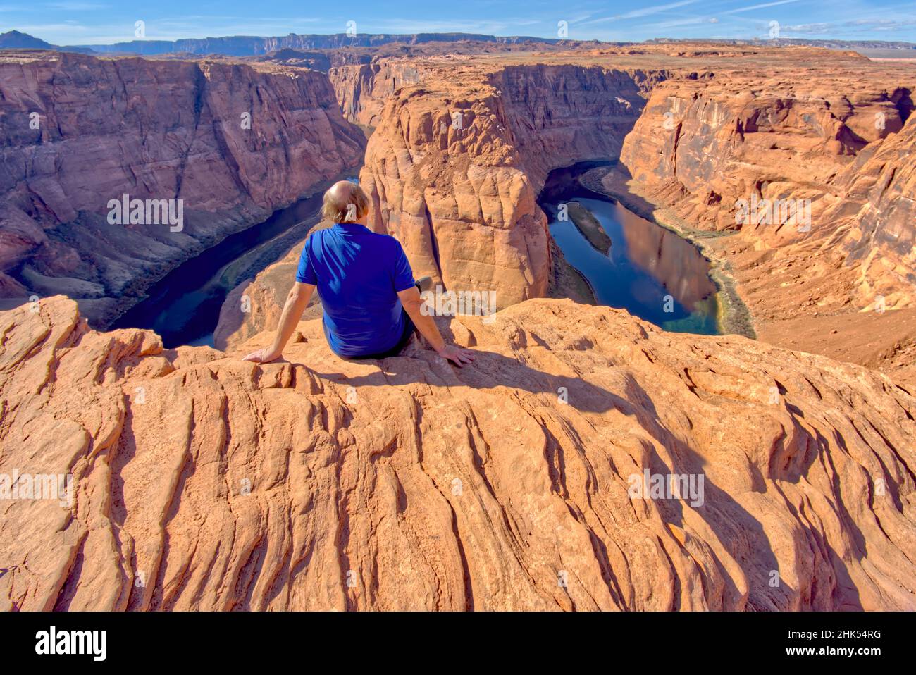 Ein Mann, der am Rand einer Klippe mit Blick auf das Horseshoe Bend in der Nähe von Page, Arizona, USA, Nordamerika, sitzt Stockfoto
