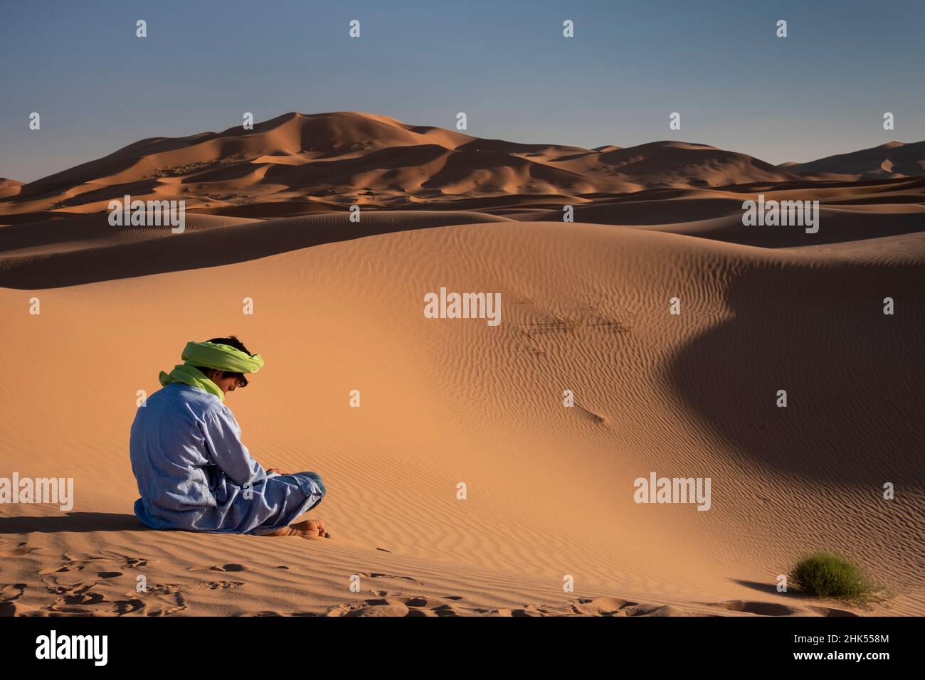 Ein Berbermann in traditioneller Kleidung sitzt zwischen den Sanddünen von Erg Chebbi, Sahara-Wüste, Marokko, Nordafrika, Afrika Stockfoto