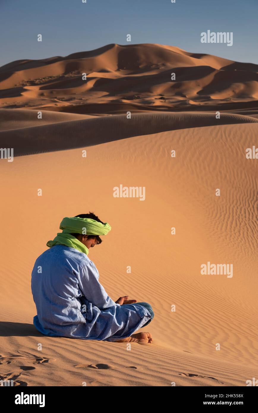 Ein Berbermann in traditioneller Kleidung sitzt zwischen den Sanddünen von Erg Chebbi, Sahara-Wüste, Marokko, Nordafrika, Afrika Stockfoto
