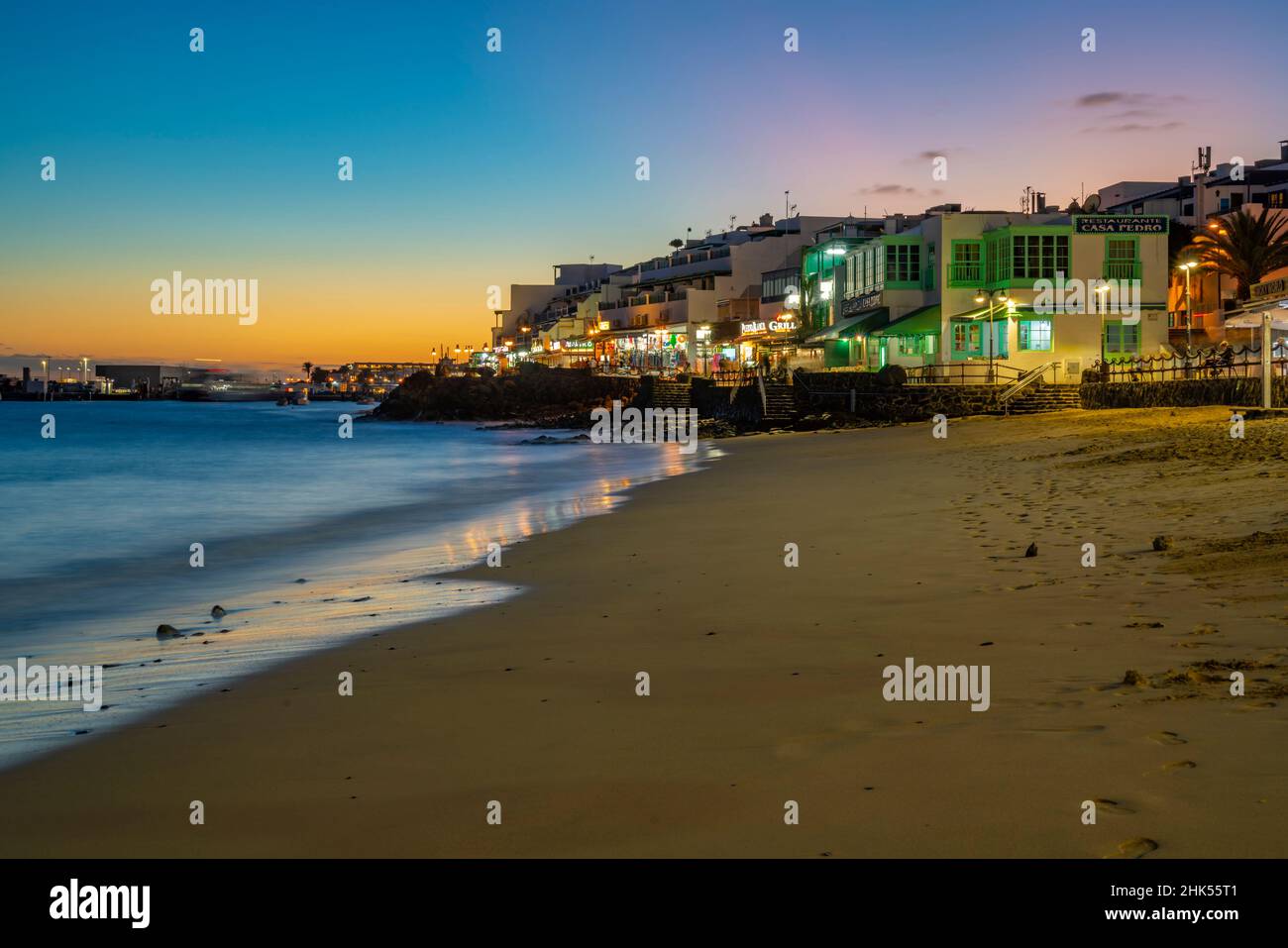 Blick auf Restaurants und Geschäfte mit Blick auf Playa Blanca Beach in der Abenddämmerung, Playa Blanca, Lanzarote, Kanarische Inseln, Spanien, Atlantik, Europa Stockfoto