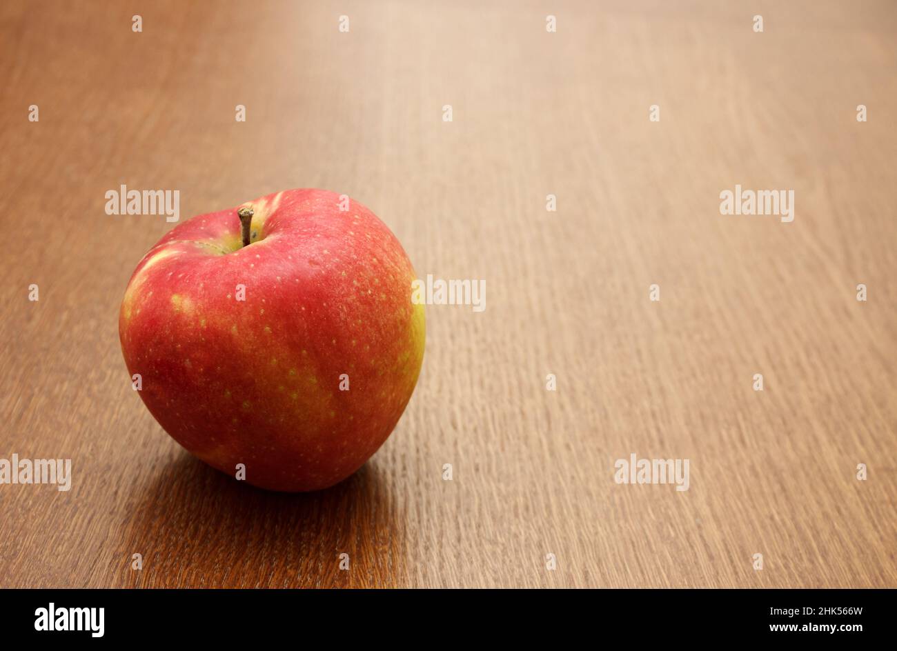 Großer leuchtend roter Apfel auf dem Tisch auf Holztisch. Nahaufnahme im Innenbereich Stockfoto