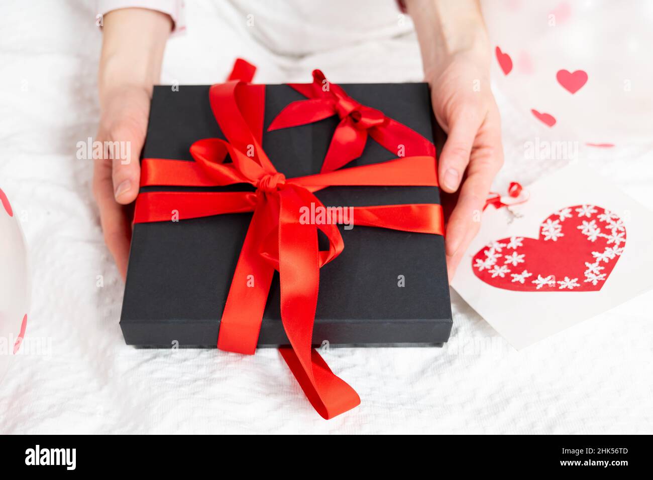 Geschenkbox verpackt und dekoriert mit einer roten schönen Schleife auf dem Bett. Valentinstag, Geburtstagsgeschenk. Jäten, Honigmooners Konzept. Liebhaber oder roma Stockfoto