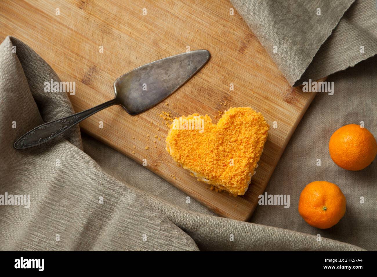 Herzförmiger Kuchen mit orangen Mandarinen auf Holztisch. Süßes Karotten-Dessert zum Valentinstag Stockfoto