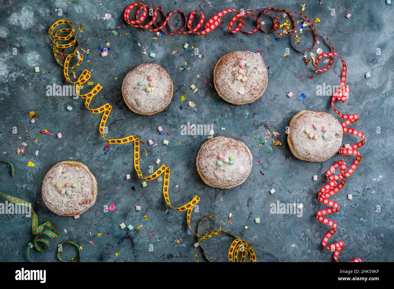 Krapfen, Berliner oder Donuts mit Streamer, Konfetti und Mini-Marschmalchen auf blauem Hintergrund. Farbenfrohes Karnevals- oder Geburtstagsbild, Draufsicht Stockfoto