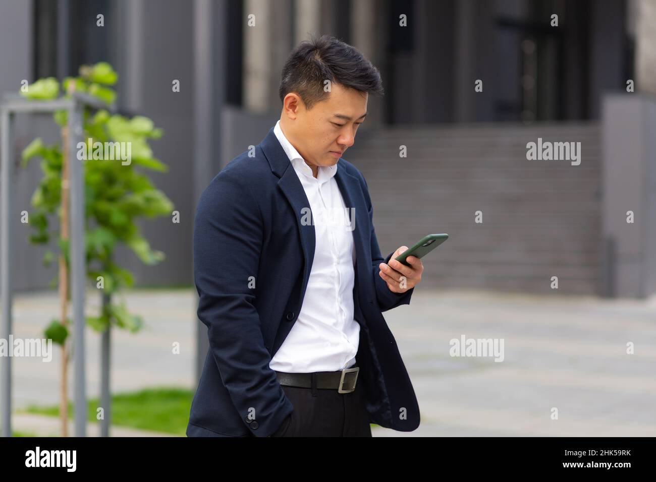 Der Chef des asiatischen Geschäftsmannes schaut auf das Mobiltelefon und liest Nachrichten vom Telefon und schreibt in einen Boten außerhalb des Büros Stockfoto