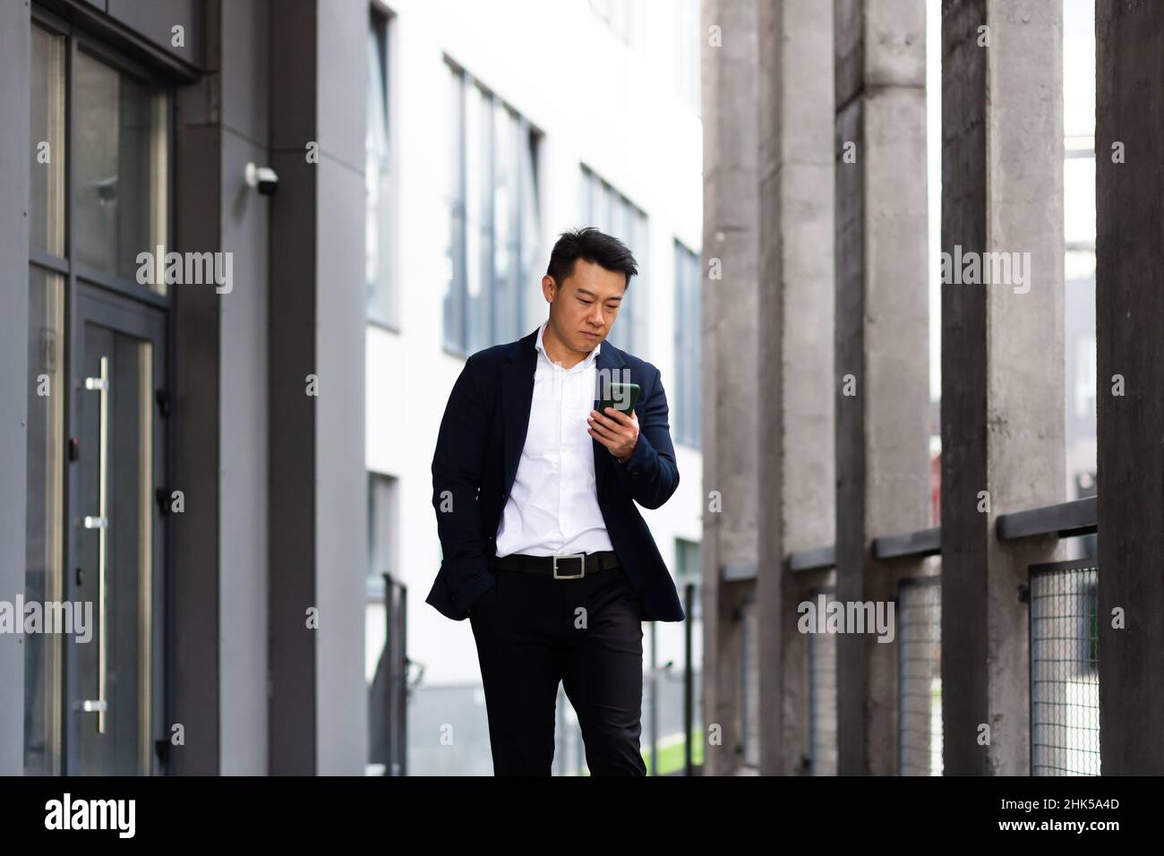 Der Chef des asiatischen Geschäftsmannes schaut auf das Mobiltelefon und liest Nachrichten vom Telefon und schreibt in einen Boten außerhalb des Büros Stockfoto