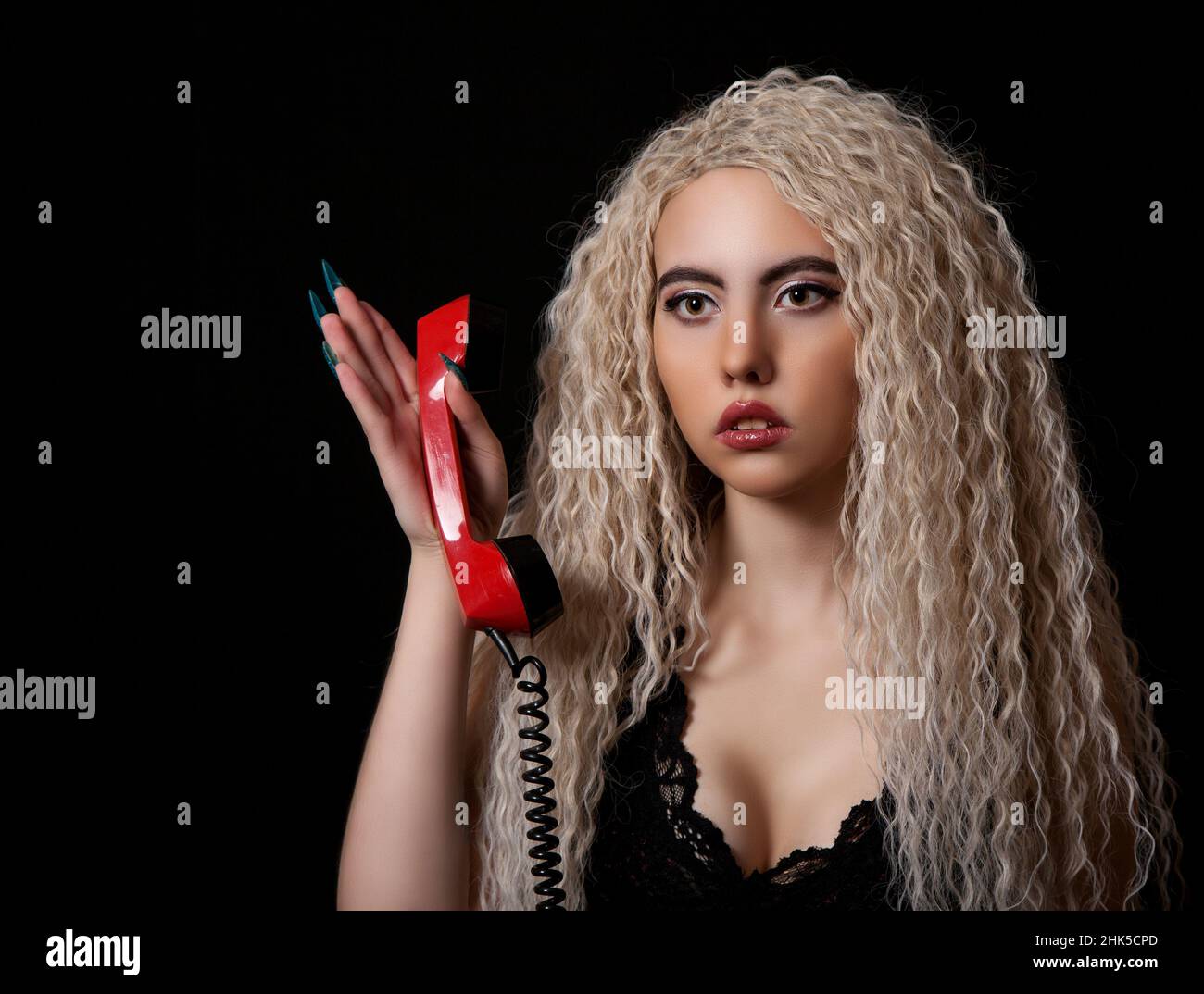 Blonde Mädchen mit langen lockigen Haaren gibt vor, eine Puppe mit einem Telefon zu sein Stockfoto