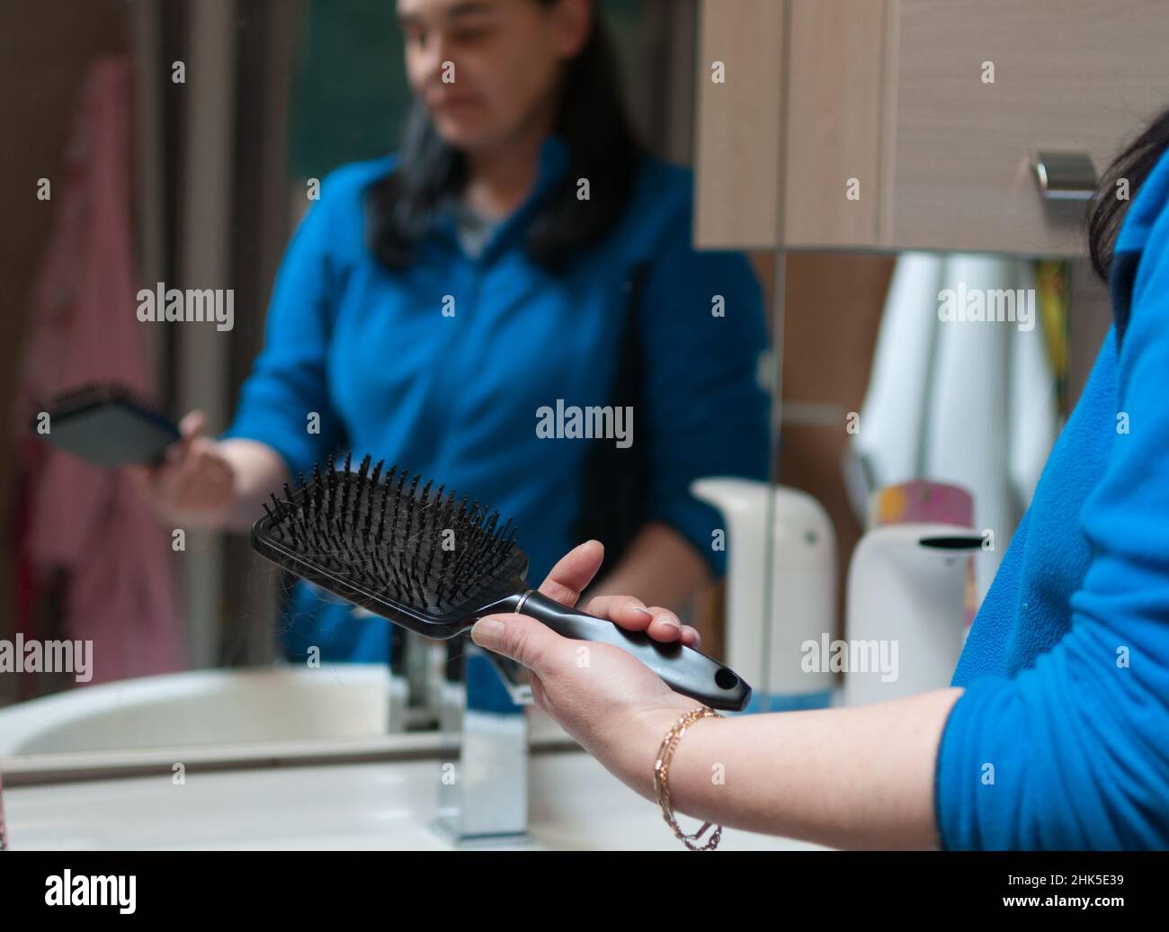 Frau schaut auf Haarbürste mit verlorenen Haaren darauf. Haarbürste im Vordergrund, Frau im Hintergrund verschwommen Stockfoto