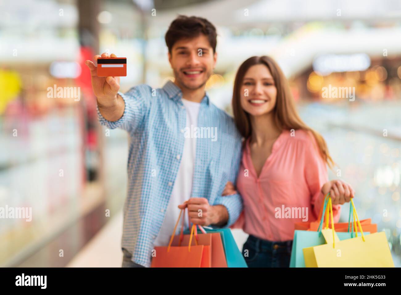 Glückliches Paar Einkaufen Und Zeigen Kreditkarte In Mall Indoors Stockfoto