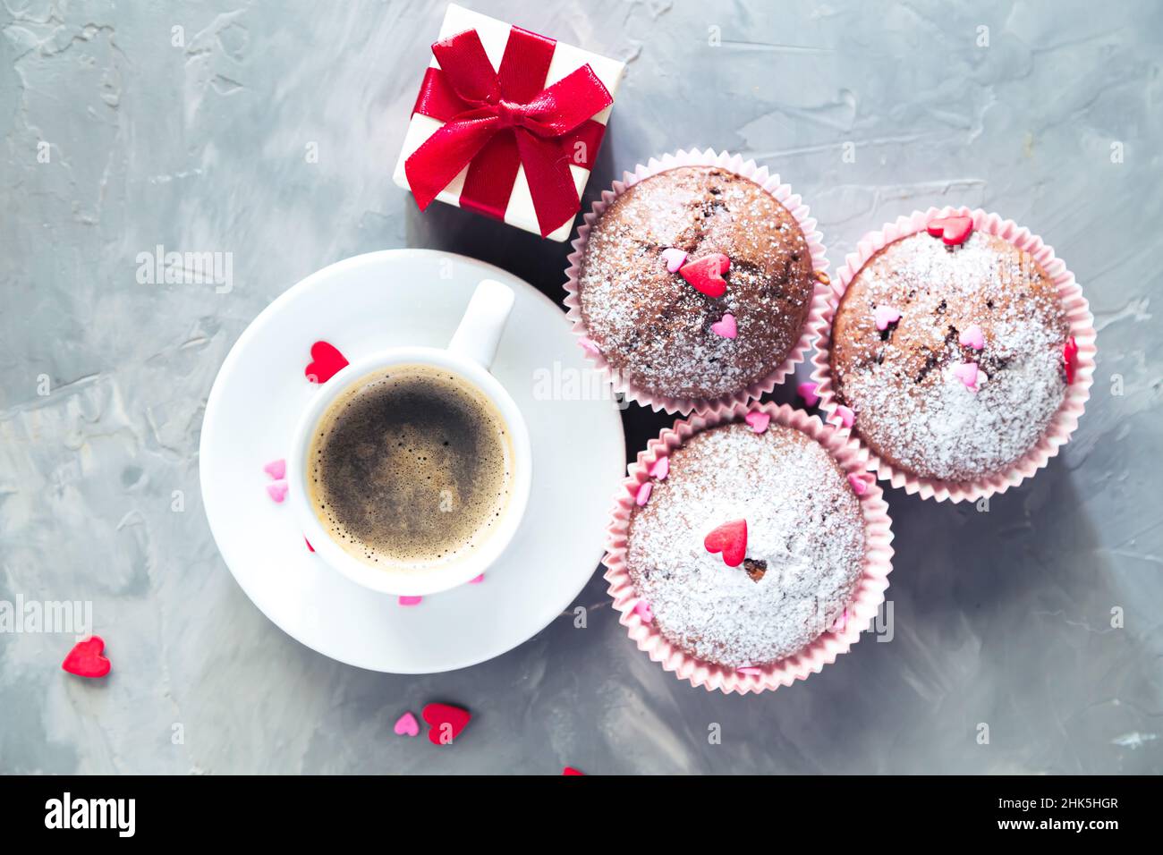 Tasse Kaffee, Schokoladenmuffins und Geschenk auf grauem Hintergrund. Das Konzept eines romantischen Morgens, Geburtstages oder valentinstag. Stockfoto