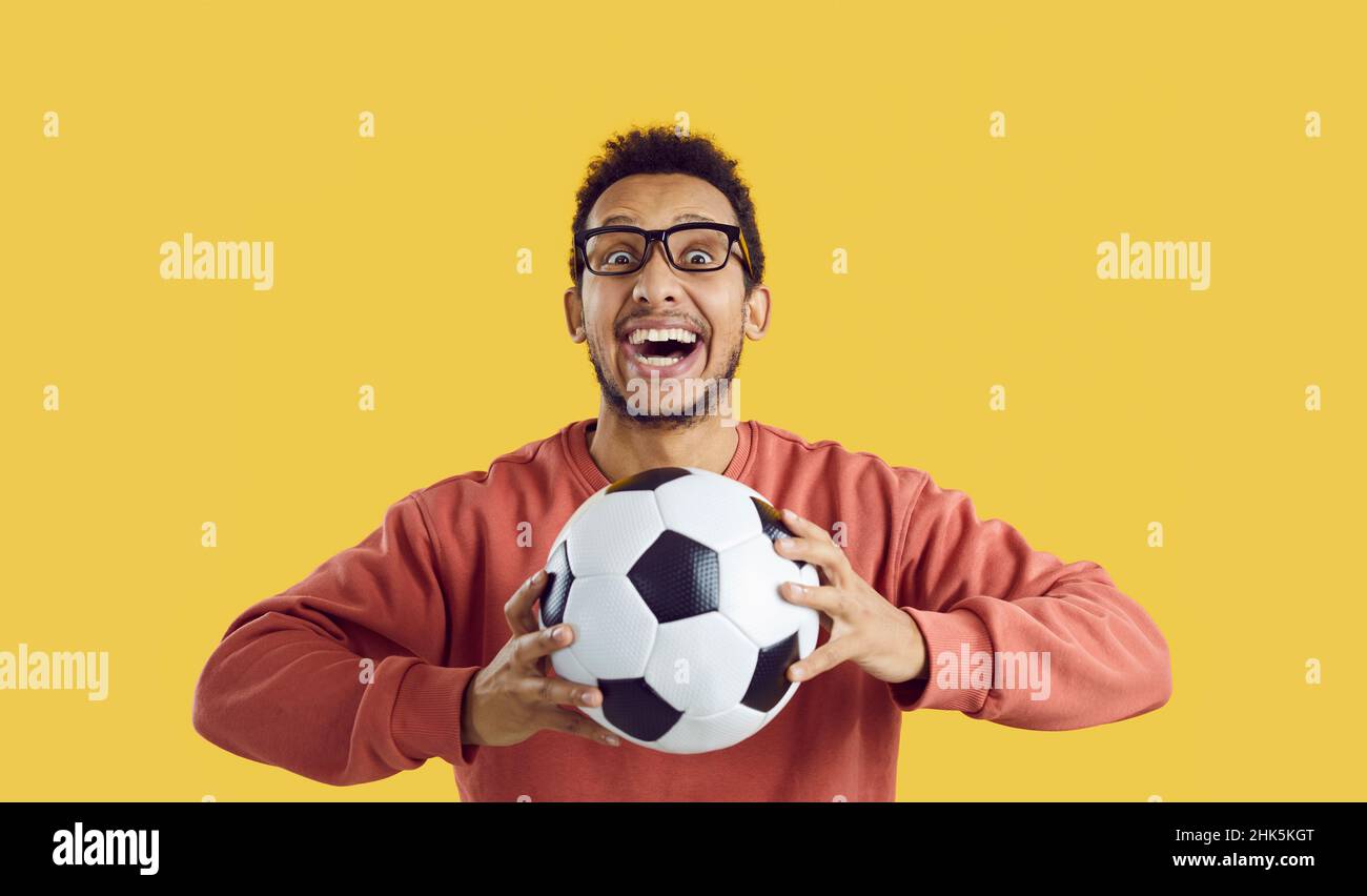 Verrückt aufgeregt Fußball-Fan hält Ball und lächelt isoliert auf gelbem Hintergrund Stockfoto
