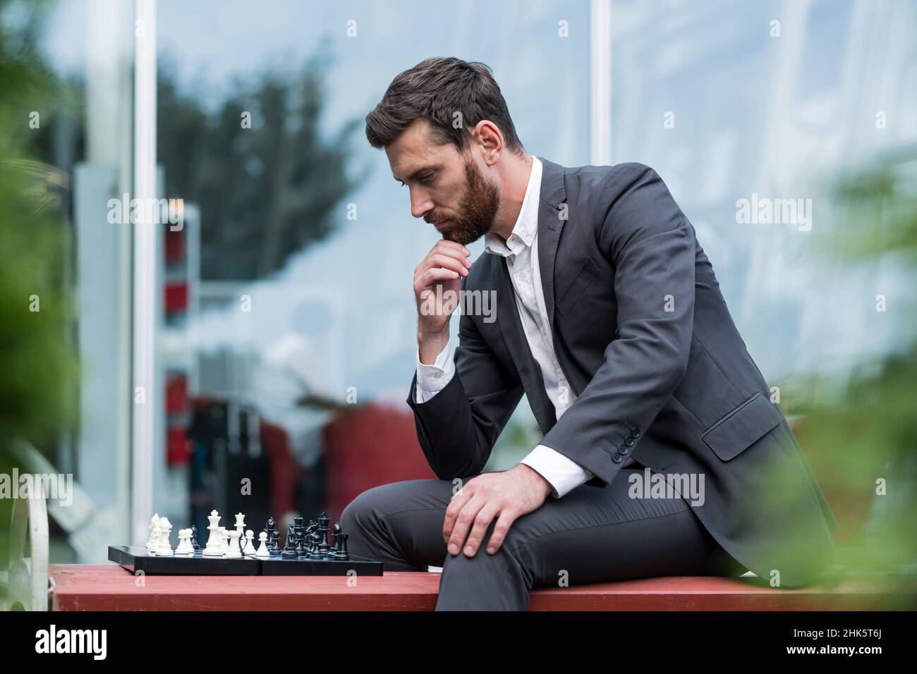 Bankier männlicher Geschäftsmann, der Schach spielt, sitzt auf einer Bank in der Nähe des Büros und macht einen strategischen Schritt Stockfoto