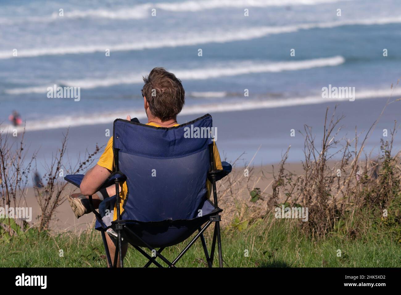 Ein Mann, der in einem Campingstuhl sitzt und auf den Fistral Beach in Newquay in Cornwall blickt. Stockfoto