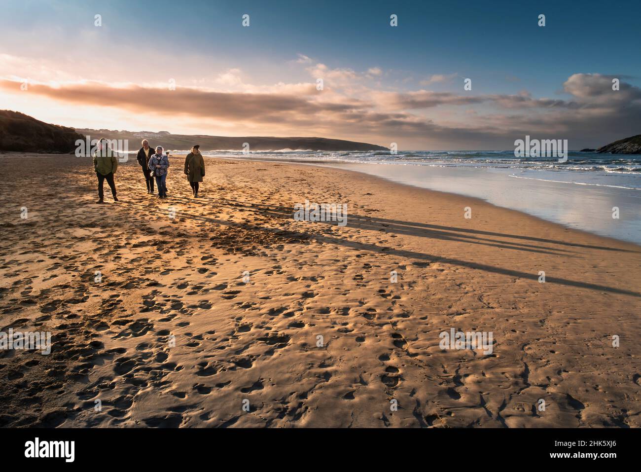 Eine Gruppe von Menschen wirft lange Schatten und genießt einen Spaziergang entlang des preisgekrönten Crantock Beach in Newquay in Cornwall. Stockfoto