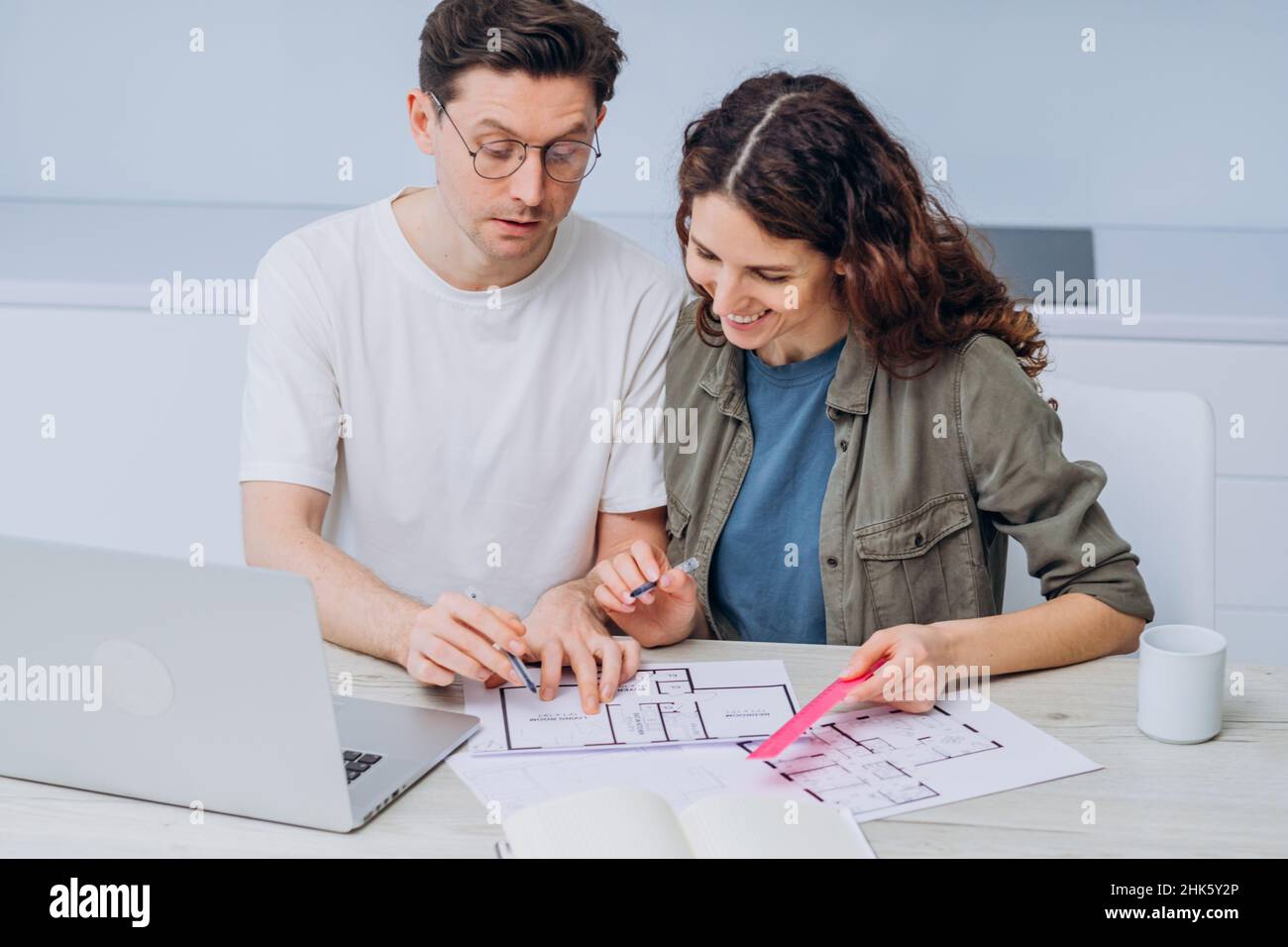 Das Paar sitzt in der Küche, trinkt Kaffee zum Frühstück und spricht über Zeichnungen von Wohnungsrenovierungen, die Notizen in Laptop und Notebook machen Stockfoto