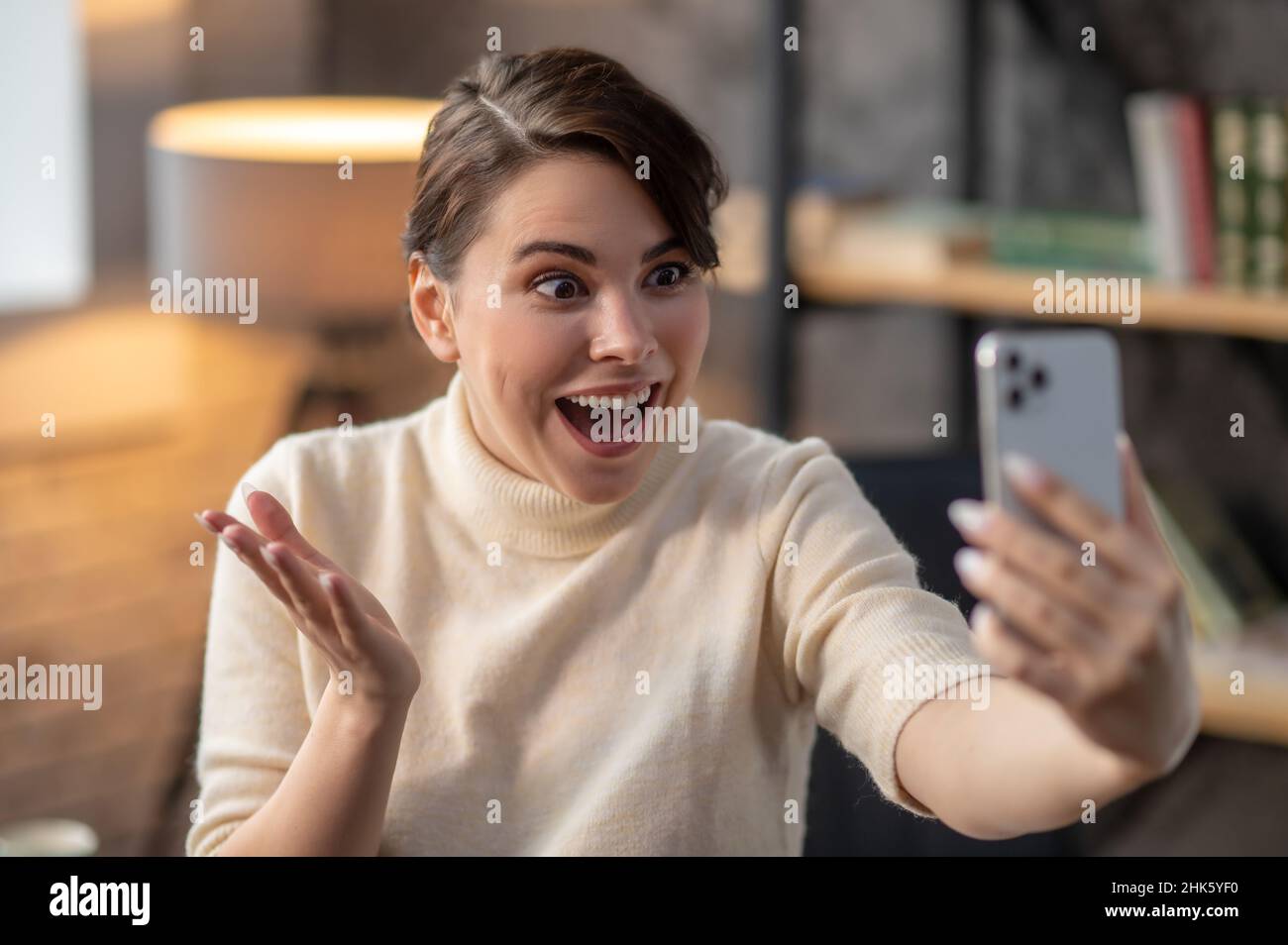 Mit offenem Mund gestikulierende Frau, die auf ihr Mobiltelefon schaut Stockfoto