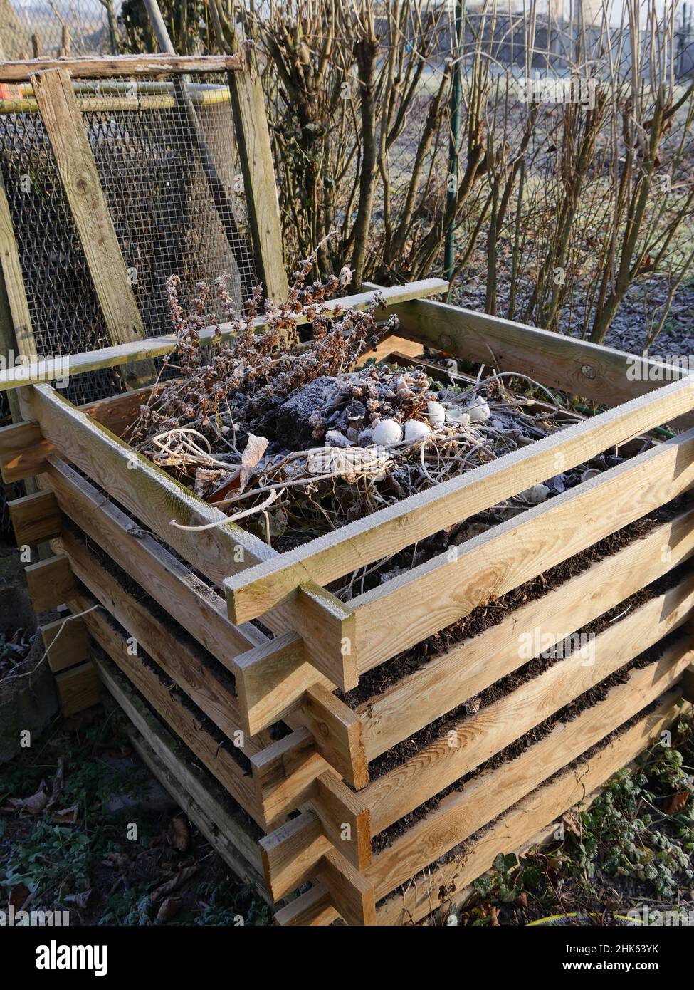 Holzkompostkasten im Winter, dahinter steht Ein Kompostsieb Stockfoto