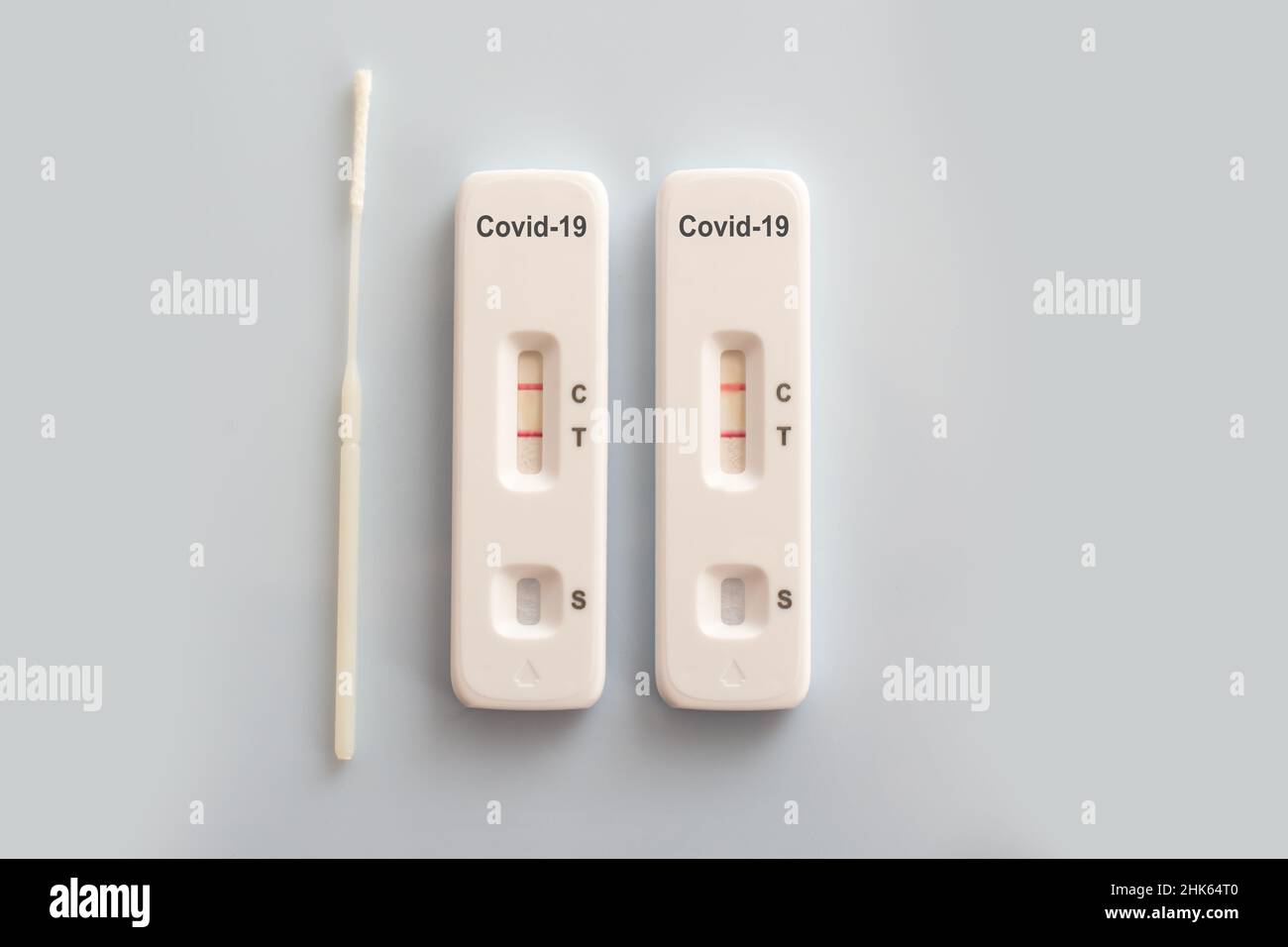 Zwei Covid-Antigen-Schnelltests und ein Nasenabstrich mit positiven Ergebnissen auf weißem Hintergrund, Covid-19-Laborkonzept Stockfoto