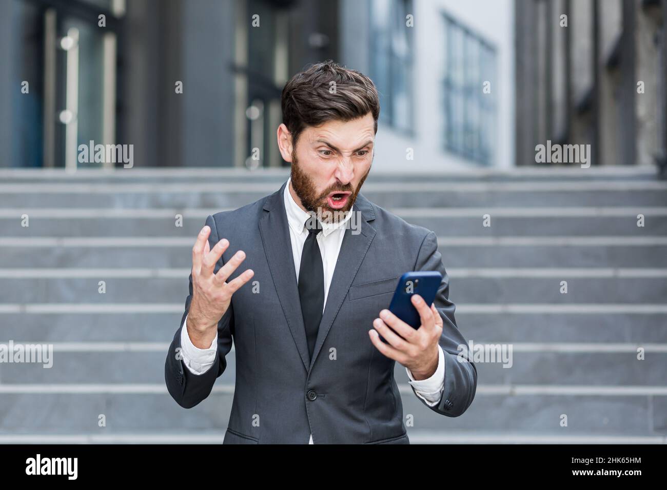Wütender männlicher Geschäftsmann weint und telefoniert vor dem Geschäftsmann, der draußen auf Anruf schreit. Nervöses, verrücktes professionelles Gespräch auf dem Smartphone. I Stockfoto