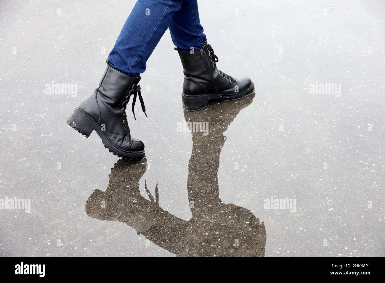 Spiegelung weiblicher Beine in schwarzen Lederstiefeln in Pfütze auf einer Straße. Regen in der Stadt, wasserdichte Schuhe für kaltes Wetter Stockfoto