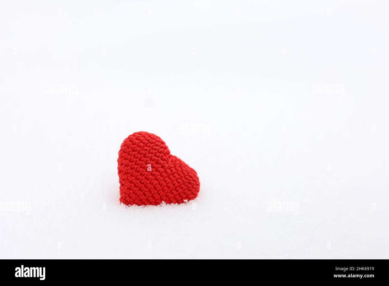Rot gestricktes Herz im Schnee. Weißer Hintergrund für Valentinskarte, romantische Liebe Stockfoto