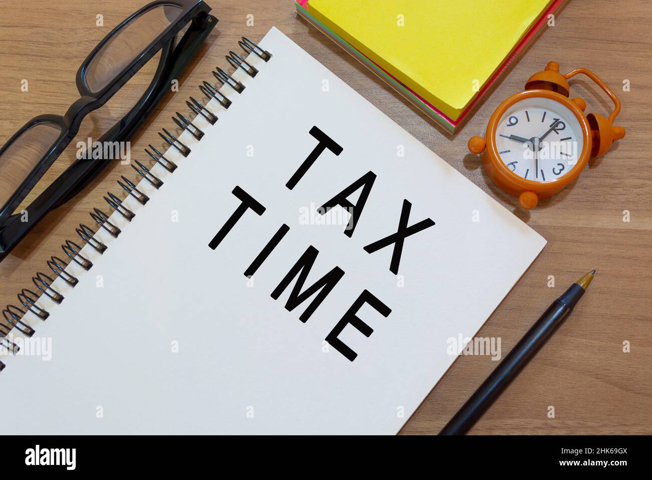 Tax Time Text auf Notizblock mit Wecker, Lesebrille, gelber Note und einem Stift auf Holzschreibtisch. Geschäftskonzept Stockfoto