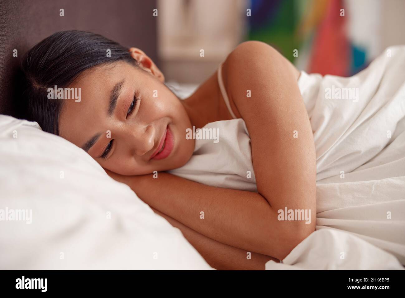 Fröhliche asiatische Frau, die zu Hause im Bett liegt Stockfoto