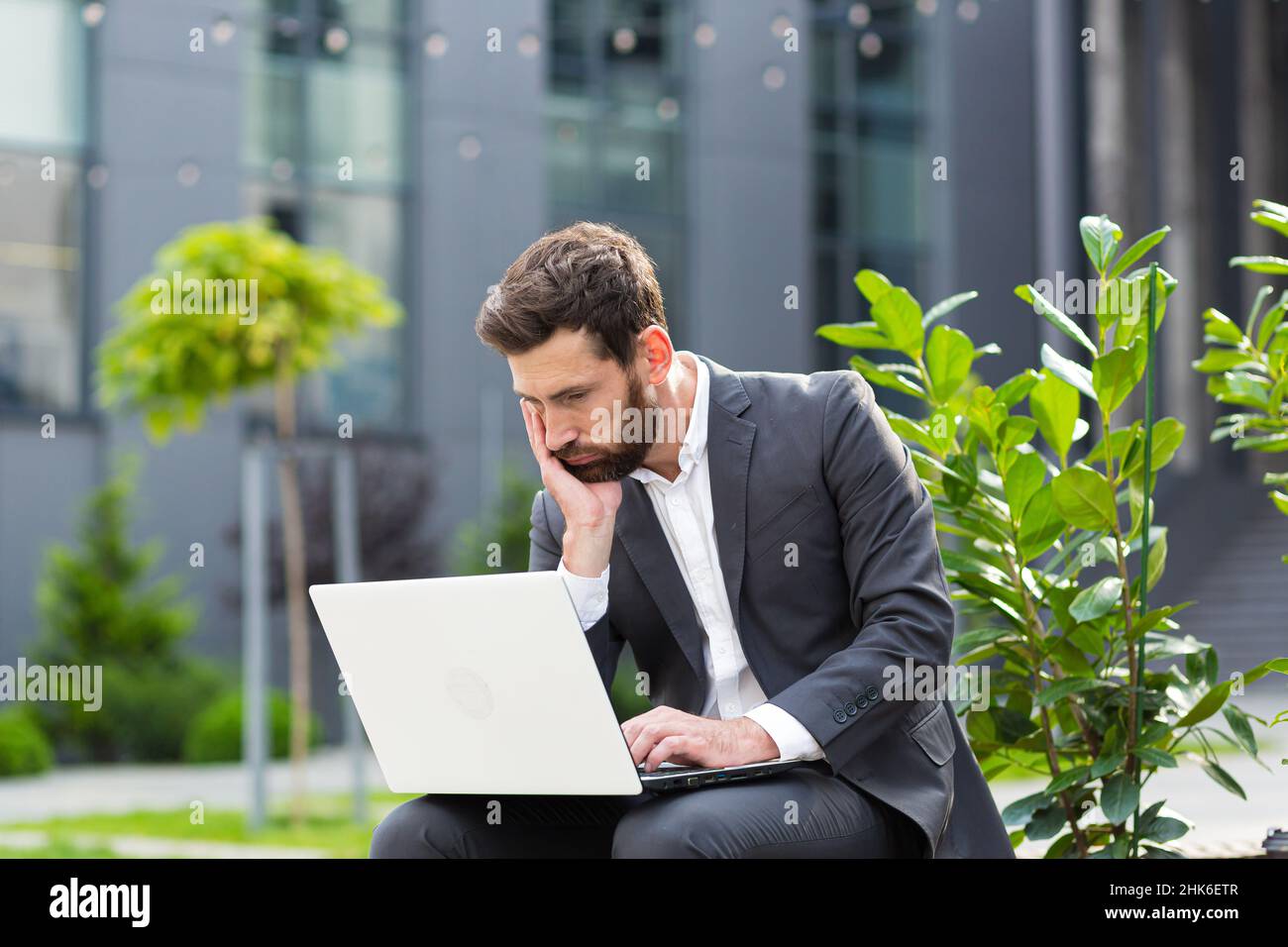 Nachdenklicher und fokussierter männlicher Geschäftsmann, der aus der Ferne am Computer arbeitet, bevor er vor dem Vorstellungsgespräch eine schwierige Entscheidung trifft Stockfoto