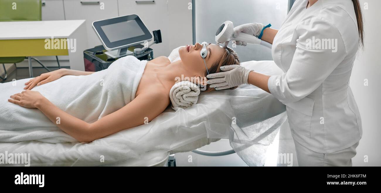 Weibliche Patientin, die Schutzbrille trägt, während der Fotorejuvenation mit intensiv gepulster Lichtintensität IPL in der medizinischen Klinik Stockfoto