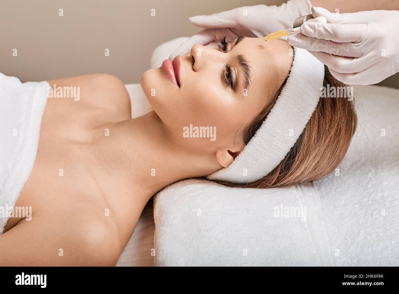 Kosmetikerin trägt Serum mit einer Pipette auf das Gesicht der Frau auf. Gesichtshaut-Pflege mit Kosmetiköl und Serum Stockfoto