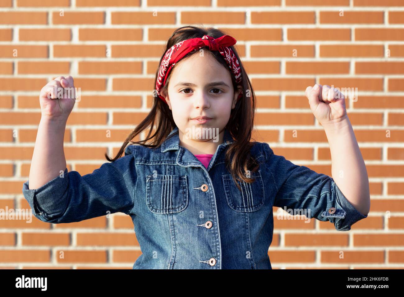 Kaukasisches kleines Mädchen, das ihre Arme mit isolierter Kraft an einer Ziegelwand beugend. Starkes Frauenkonzept. Stockfoto