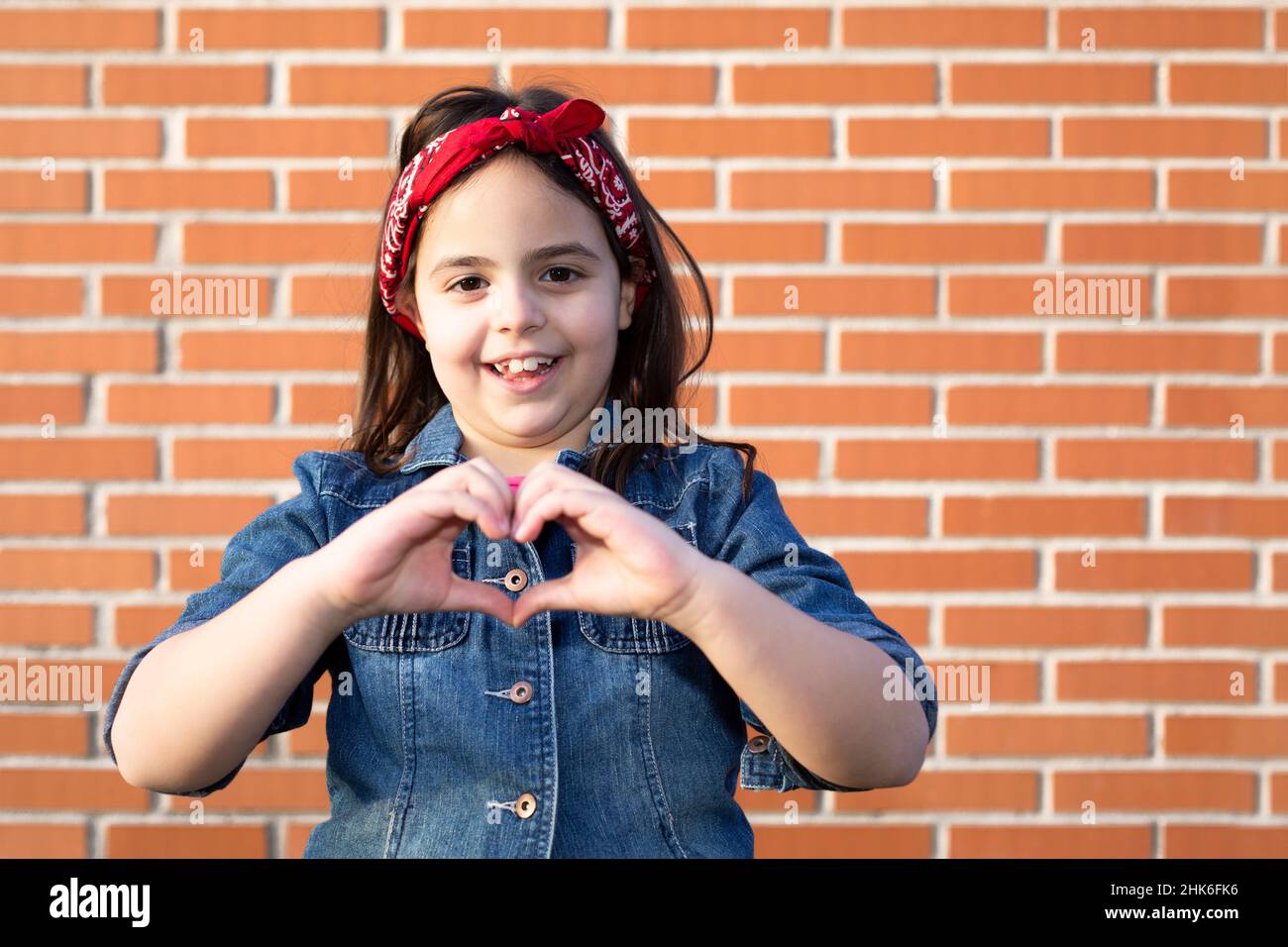 Kleines aktivistisches Mädchen, das Herz formt, wobei ihre Hände auf einer Ziegelwand isoliert sind. Liebe und feministische Zukunft. Platz für Text. Stockfoto