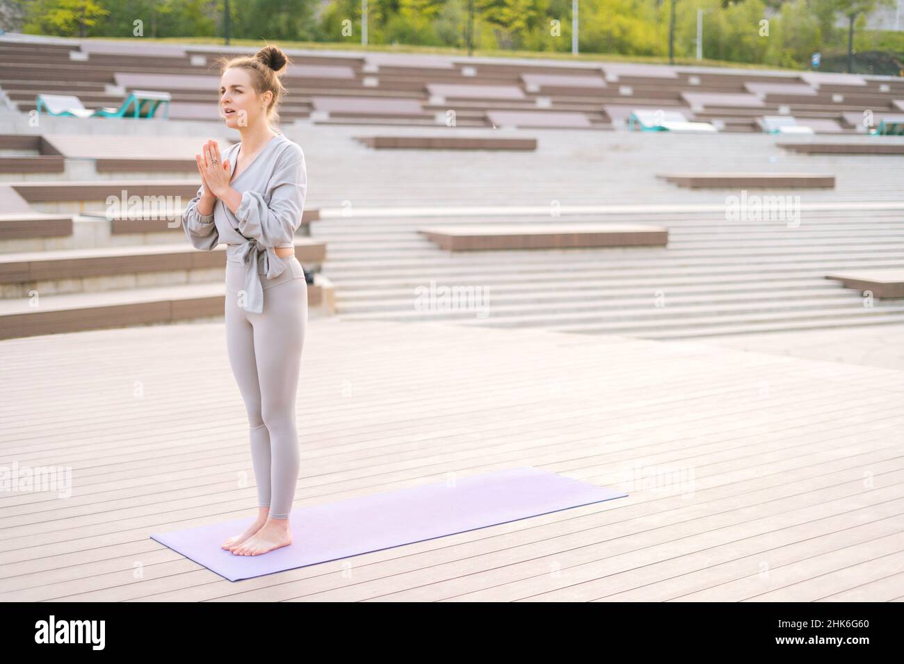 Weite Aufnahme einer ruhigen, attraktiven kaukasischen jungen Frau, die Yoga praktiziert und im Stadtpark eine Namaste-Pose durchführt. Stockfoto