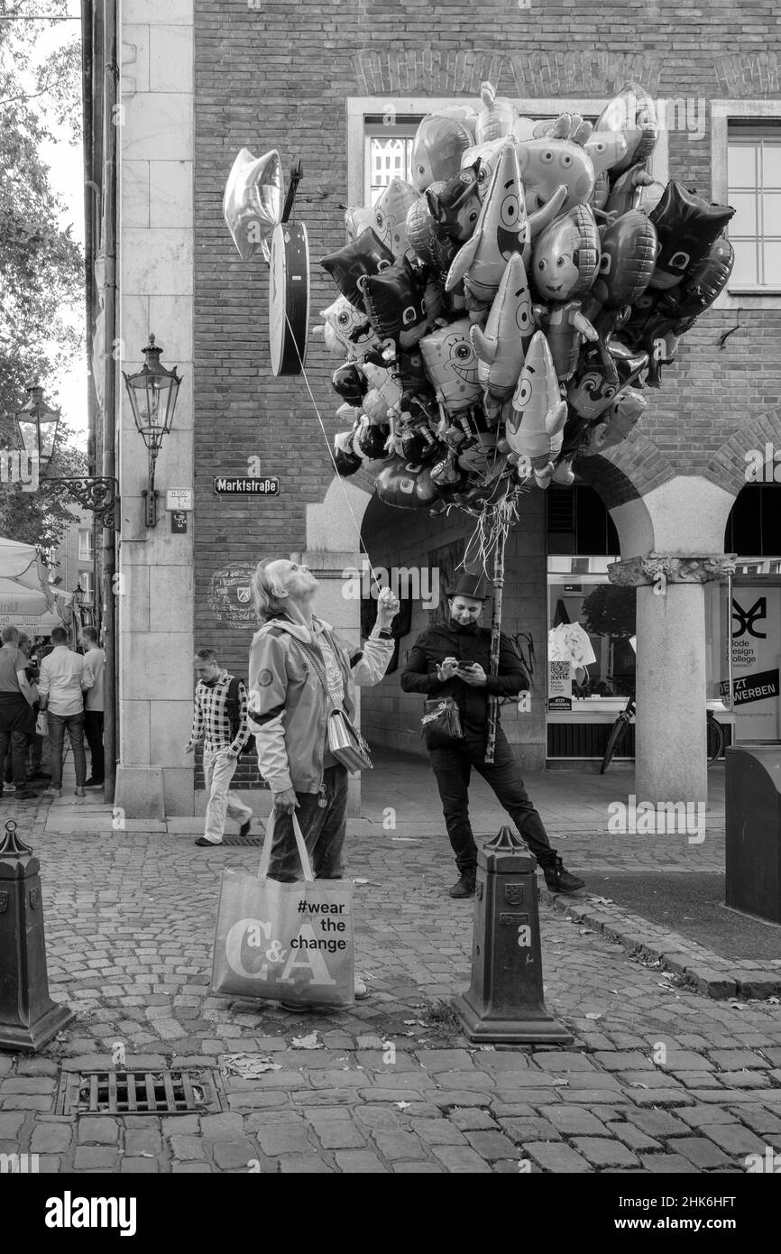 Ein Mann schaut auf seinen schwebenden sternförmigen Ballon, während ein als Schornsteinfeger gekleideter Ballonverkäufer auf seinem Handy in der Düsseldorfer Altstadt unterwegs ist Stockfoto