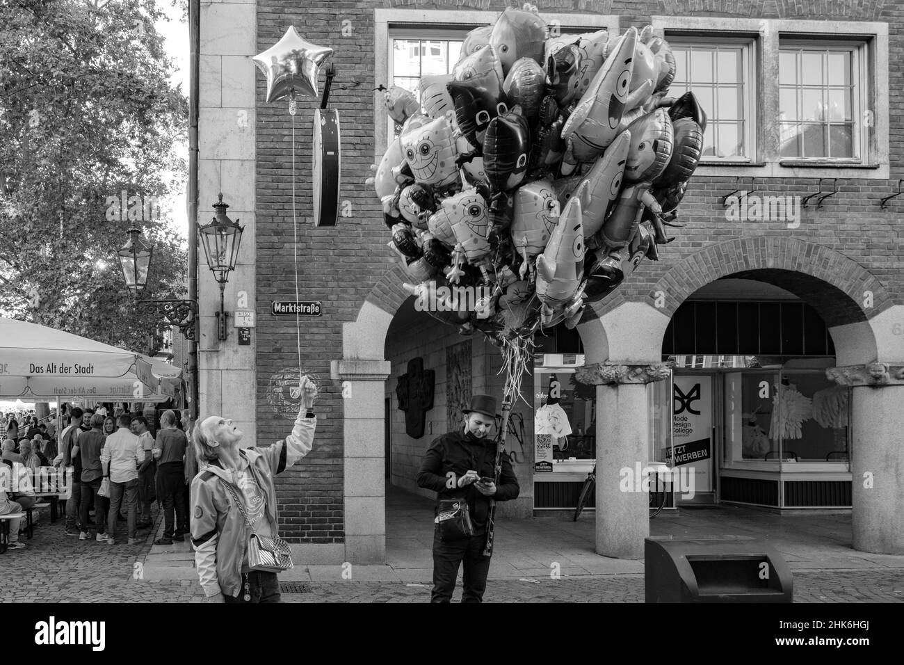 Ein Mann schaut auf seinen schwebenden sternförmigen Ballon, während ein als Schornsteinfeger gekleideter Ballonverkäufer auf seinem Handy in der Düsseldorfer Altstadt unterwegs ist Stockfoto