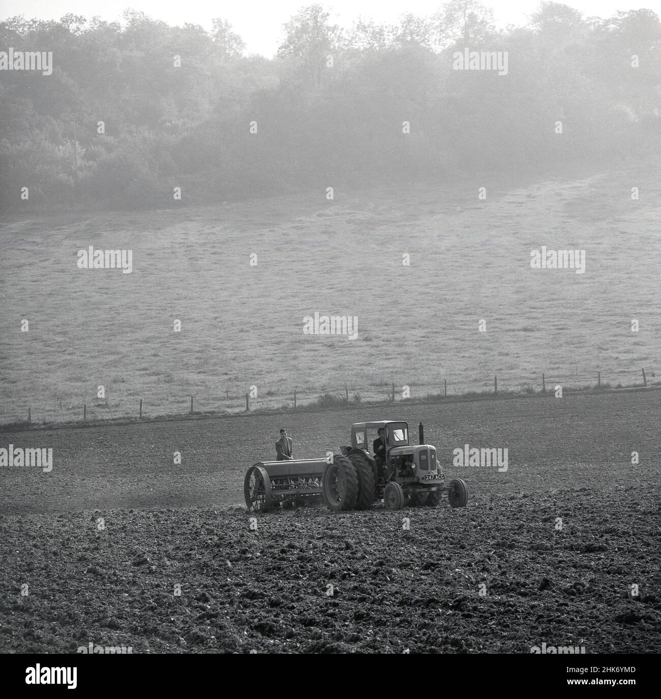 1950s, historisch, landwirtschaftlich, auf einem Feld auf einer Farm am Hang, zog ein Mann, der einen Aufzug auf der Rückseite eines Massey-Pfluges anbrachte, hinter einem Nuffield Universal-Traktor, England, Großbritannien, einen in Großbritannien hergestellten Traktor von Morris Motors in den Nachkriegsjahren. Stockfoto
