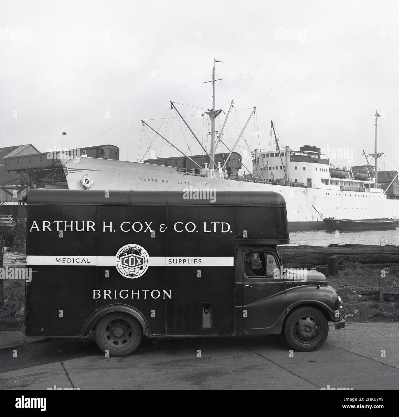 1950s, historisch, ein Lieferwagen von Arthur H. Cox & Co aus Brighton, England, UK in Austin. Geparkt in London legt am Hafen von London an. Das britische Unternehmen wurde 1839 von Arthur Hawker Cox gegründet und war in dieser Zeit ein führender Hersteller und Hersteller von medizinischen Hilfsmitteln, der seine Tabletten und Tabletten in die ganze Welt exportierte. Auch an den Docks, das norwegische Frachtschiff, 'Nördliche Lichter'. Stockfoto